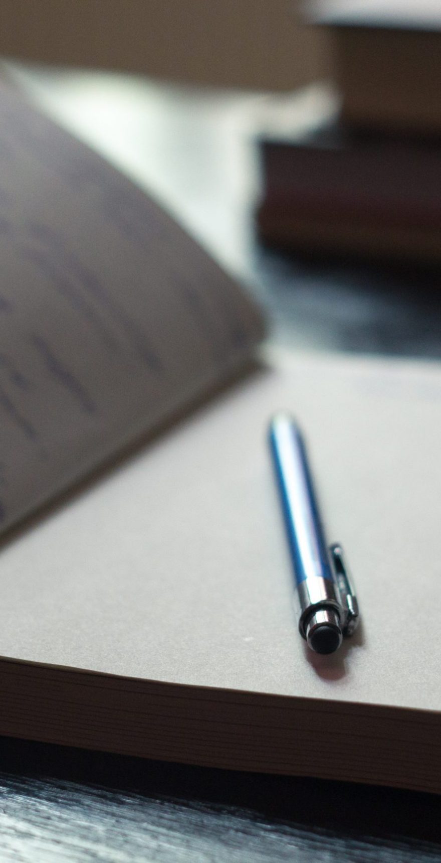Open Notepad with handwritten notes with blue pen, books in the background Open Notepad with handwritten notes with blue pen, books in the background
