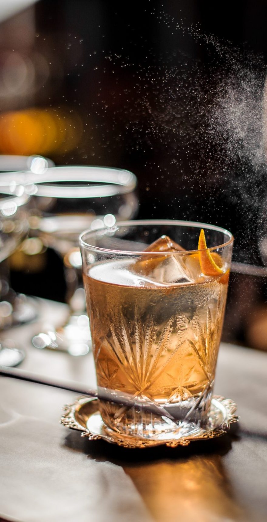 Bartender decorating fresh old fashioned summer cocktail with ice and orange peel Bartender decorating fresh and tasty old fashioned summer cocktail with ice and orange peel on the vintage brown background