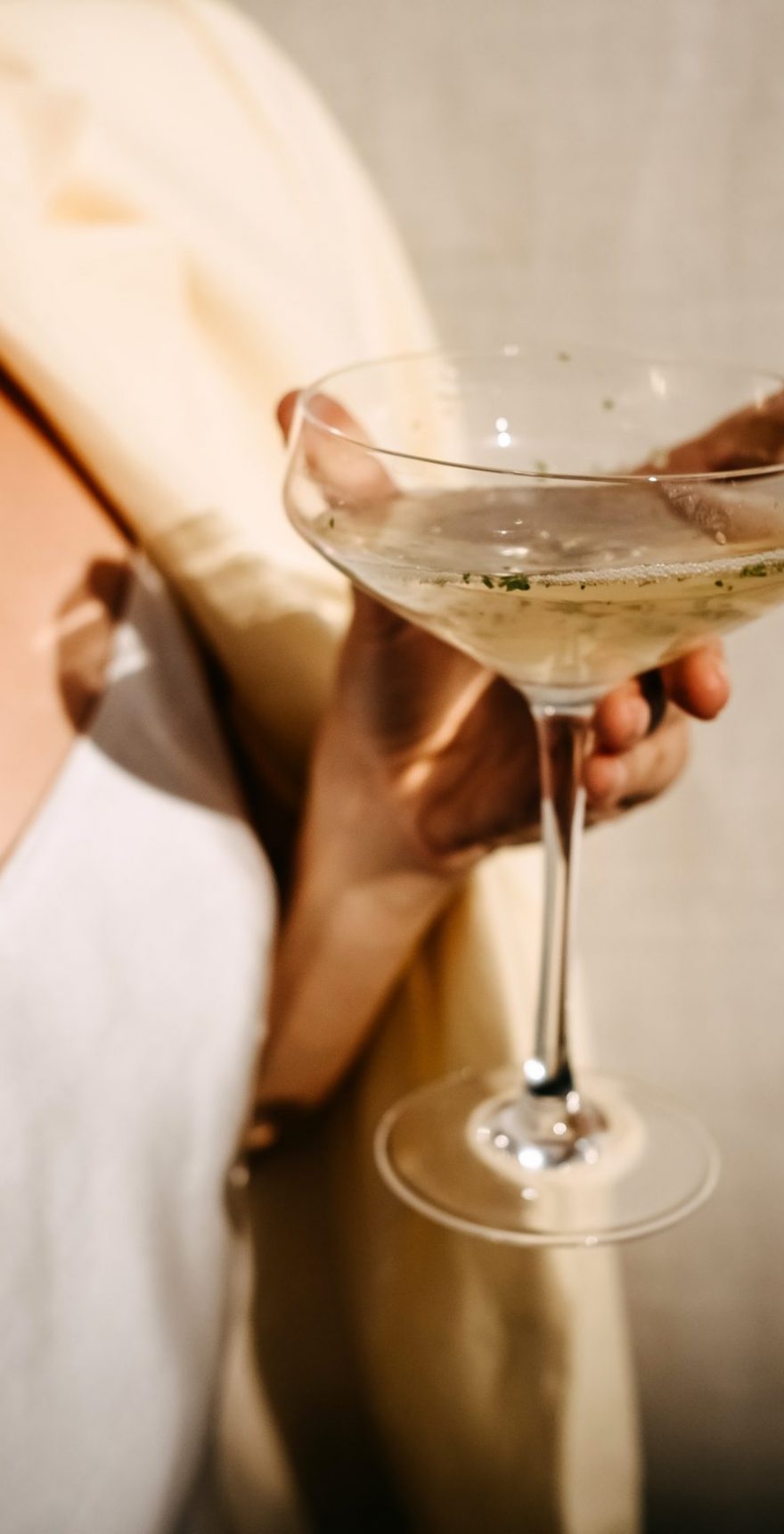 Woman dressed in white dress holding a coupe with a cocktail in sun light. Concept of an open air party. Woman dressed in white dress holding a coupe with a cocktail in sun light. Concept of an open air party.